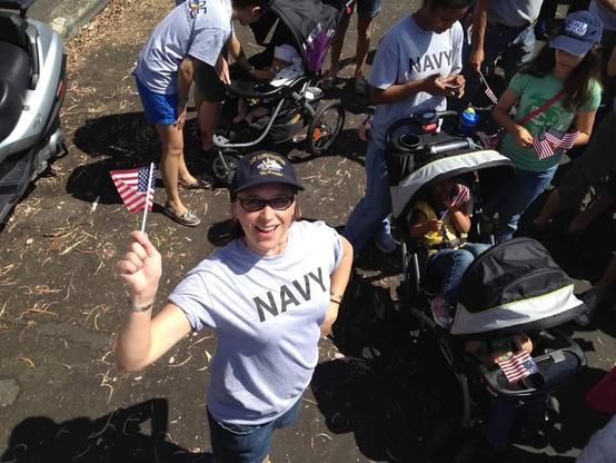 Kari in a grey tee shirt with "Navy" on it, holding a small American flag in the San Diego Pride Parade.