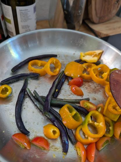 Tomatoes, beans, and orange pointy peppers in a pan.