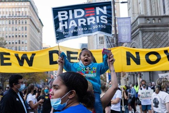 A young child on parent's shoulders holding up a Biden Harris sign in 2020.