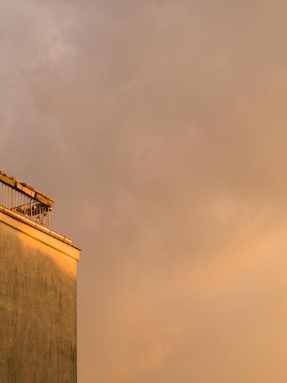 Dirty yellow clouds of an approaching thunderstorm. On the left, the edge of a building with a terrace on top. The facade of the building is yellow, too.