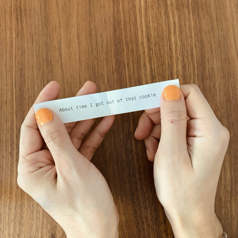 Hands holding a piece of paper like those from fortune cookies that says: about time I got out of that cookie