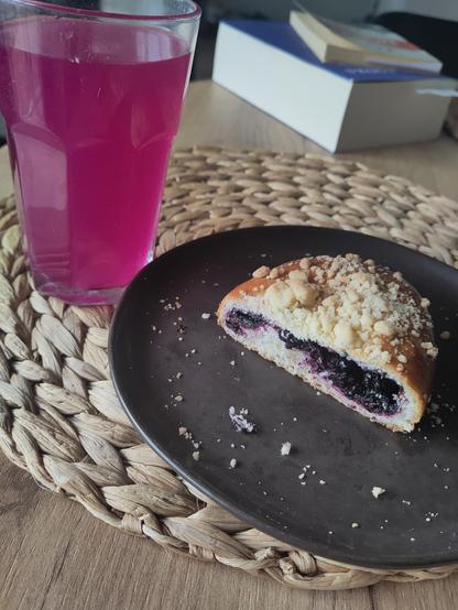 A glass with bright pink fluid, almost radioactive looking. A plate with half a bun, cut open so that the inside is revealed, which is a blueberry filling.
