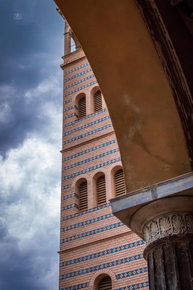 Bell tower of Romanesque church against a dramatic cloudy sky as seen through the arches of the church portico. Church of the Redeemer, Sacrow, Potsdam, 23 Jul 2024. Nikon D5600, Nikkor DX 35 mm ƒ1.8G, ISO 3600, ƒ22, -0.3 ev, 1/125s, polarizing filter