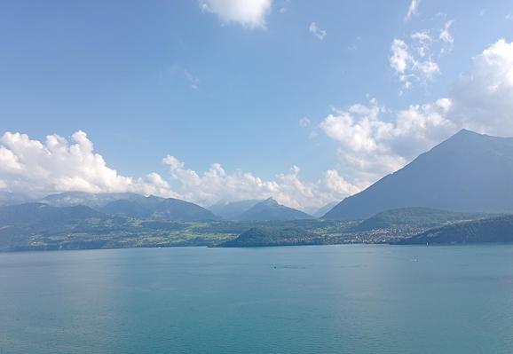 Im Vordergrund der See. Dahinter die Berge, recht der Niesen. Darüber blauer Himmel und weisse Quellwolken.