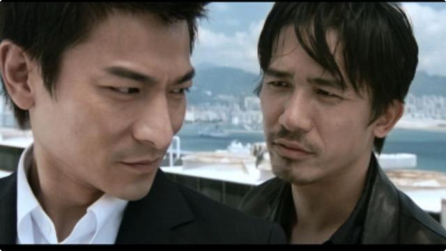 Two men are seen in close proximity on a rooftop, with one wearing a suit (Andy Lau) and the other a leather jacket (Tony Leung), against a Hong Kong cityscape background. They both appear to be in a serious or intense conversation.