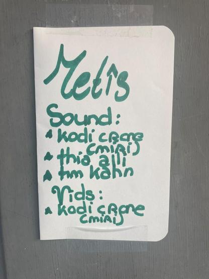 A handwritten sign in marker taped to a gray wall for a audio/visual installation.