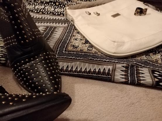 A closer view of studded detail on boots, tribal style pattern of fabric, while the earrings, ring, and white bag are also in view.