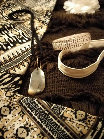 A closer view of the snow jasper pendant, the fluffy brown poncho's knitted pattern and the text on the acrylic bangle, while the bag's strap, dress fabric and flower hair clip are also in view.