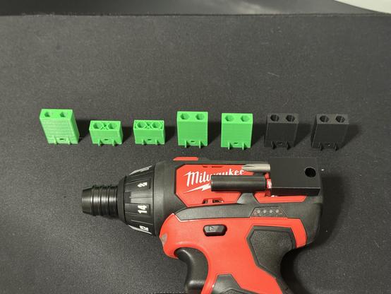 A battery-powered screwdriver with a customized bit holder attached. Along the side, there are 7 bit holders that were printed during the design iterations.