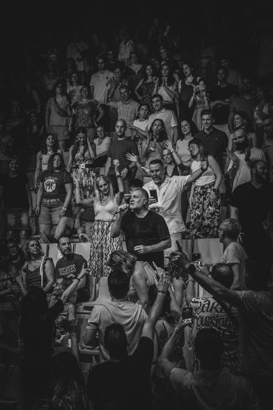 Fotografía en blanco y negro donde se ve al cantante de La Habitación Roja subido entre el público del auditorio de Pui Pinos (Alcañiz) y cantando entre ellos.