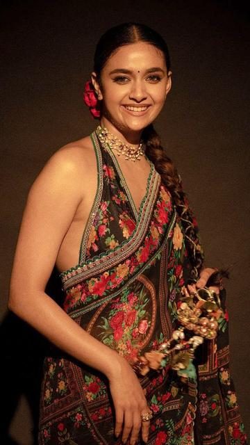 Keerthy Suresh captivates in a black floral saree that exudes charm and sophistication. The vibrant floral design on the saree is both eye-catching and elegant, perfectly complementing Keerthy's graceful demeanor. Her fashion choice highlights the beauty of combining classic black with colorful floral accents. This stunning outfit is ideal for those looking to make a bold yet refined fashion statement. Discover the allure of Keerthy's look and add a touch of elegance to your wardrobe.