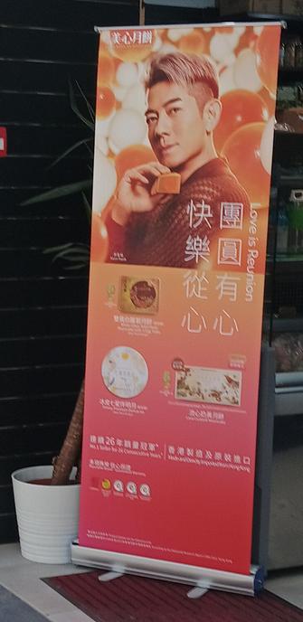 An orange and red standee advertising mooncake. There is a Chinese man holding one up to his face suggestively. I guess he is famous and people think he is sexy.