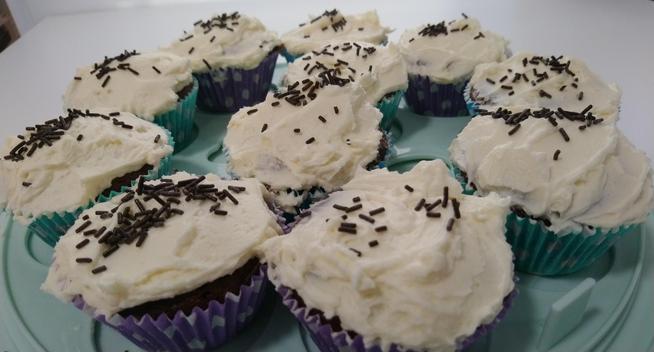 Closeup of 11 chocolate cupcakes with icing and chocolate sprinkles.