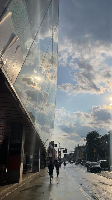 After rain, sun shines on glass reflecting sky and clouds, cool mirror effect, shiny pavement, some silhouettes of people walking