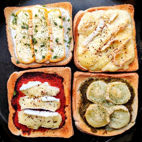 Une photo carrée, dans un plat noir anti-adhésif qui prend tout l'écran il y a 4 toasts de pain de mie :

En haut à gauche, du fromage roux en tranches verticales sur du fromage blanc à l'ail, le toast est saupoudré de ciboulette.

En haut à droite : des tranches de reblochon au lait cru en diagonale sur un lit de moutarde. Le toast est saupoudré avec un peu de flocons de piment coréen rouge.

En bas à gauche, le toast a reçu une sauce huile d'olive et concentré de tomate, ainsi que 3 morceaux de Brie posés à l'horizontale. Le toast est saupoudré de piment coréen rouge qui donne une agréable chaleur.

En bas à droite, 4 tranches de chèvre bûche se sont alanguies sur un lit de pesto. Elles sont saupoudrées de persillade. 

Le pain est doré et on le devine croustillant. L'image est une invitation à choisir votre toast préféré ! (Où à les dévorer tous 🤭)