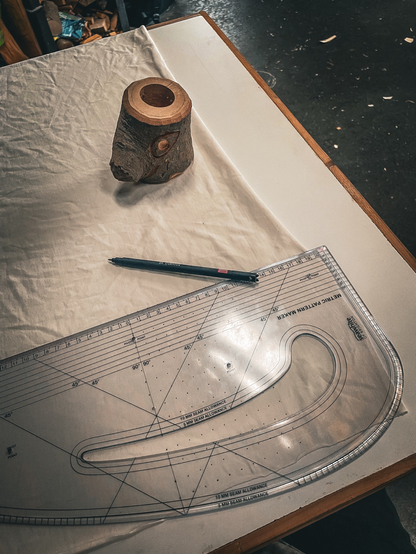 A ruler on top of some fabric with a pen, a small carved wood face acts as a weight. 