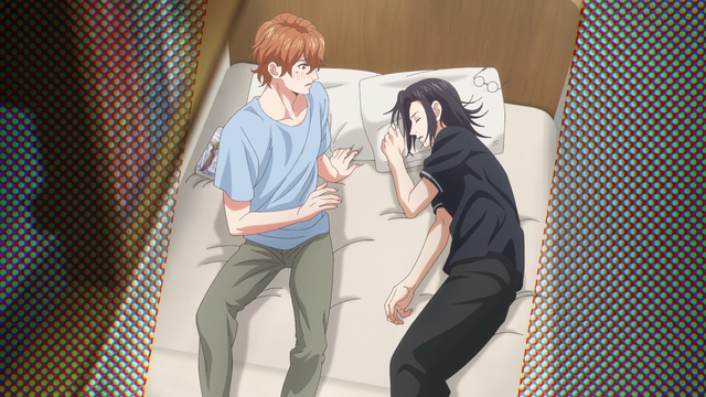 A teenage boy (Kikuchihara) looks with a blushed face at a teenage boy (Gichi) sleeping next to him in a bed.