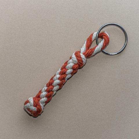 A photograph of a bellrope-style keychain pendant, tied in 3mm cotton cord in rust-brown and off-white.
