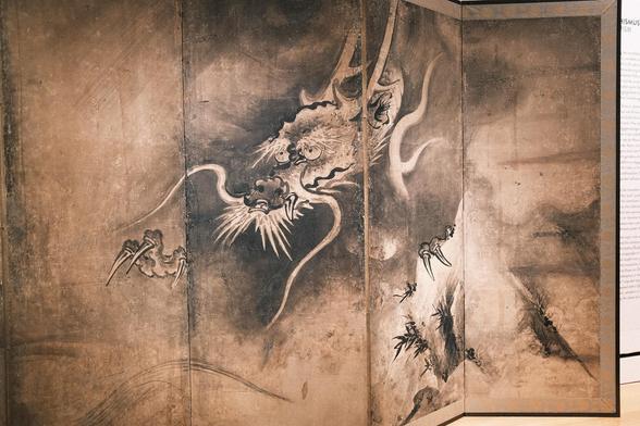 Dragon and Tiger (detail), attributed to Tosa Mitsutsugu (active ca. 1624-1644), pair of six-fold screens (byōbu), ink on paper Japan, first half 17th century. Tiger and dragon symbolize the duality of heaven and earth. In China, their cosmological meaning referred to the eastern and western directions, spring and fall, rain and wind, and the elements of wood and metal. In Japan, the dragon and tiger are associated as a pair with two hanging scrolls dated 1269 by the Chan monk painter Muqi in the possession of Daitoku-ji in Kyoto. , Here, the placement of the dragon on the right and the tiger on the far left creates an exciting space in between. Diagonally swept brushstrokes suggest rain in the dragon depiction, while the waving bamboo leaves in the tiger picture suggest wind. Seen in an exhibition at the Museum für Ostasiatische Kunst, Cologne, in August 2024.