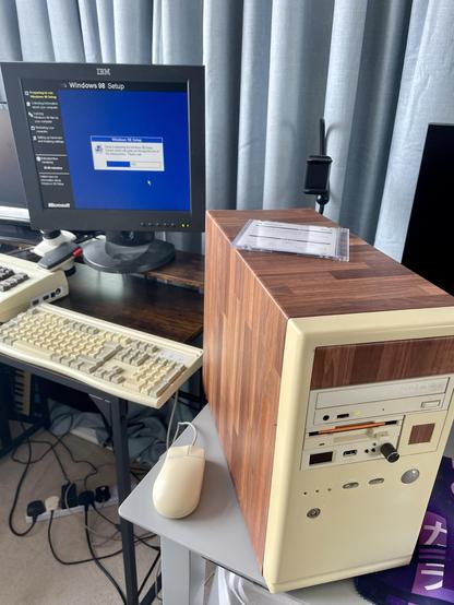 An old PC in a tower case with a wood grain effect. The screen shows Windows 98 being installed.