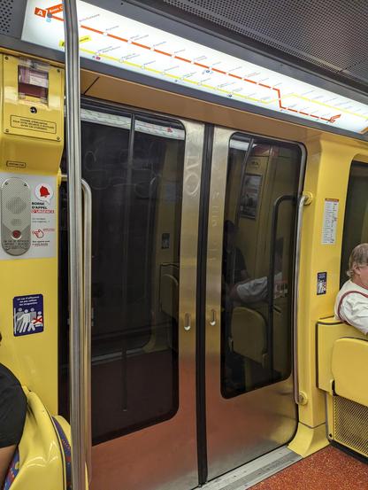 Porte d'une rame de métro toulousaine prise depuis l'intérieur. Entourée des parois en plastique en jaune. Au dessus de la porte les itinéraires de ligne.