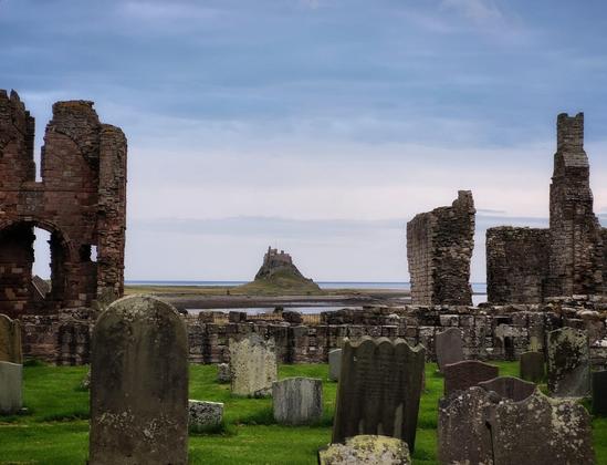 The view of Lindesfarne Castle from the graveyard of St Mary's church. Lindesfarne priory frames the shot