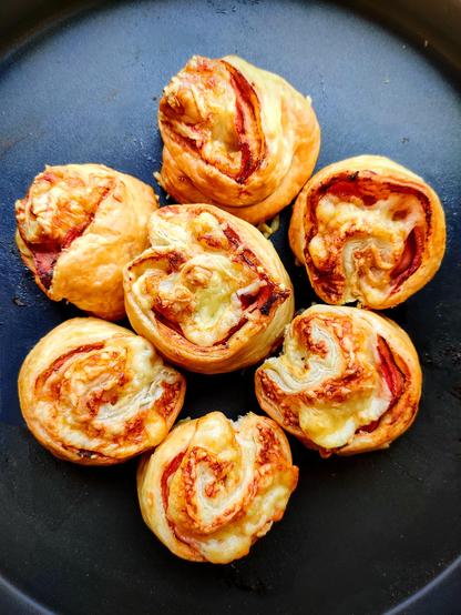 Au centre d'un plat noir antiadhésif on voit 7 feuilleté au jambon, au fromage et à la moutarde qui sont bien dorés. On peut voir sur leur dessus la spirale avec le jambon et le fromage. Ils sont rassemblés en fleurs mais ne sont pas collés les uns aux autres. Le résultat est bien croustillant, goûtu, et grâce à la manière de plier la pâte ils ne sont pas trop inégaux en taille bien que la pâte soit ronde à la base. 