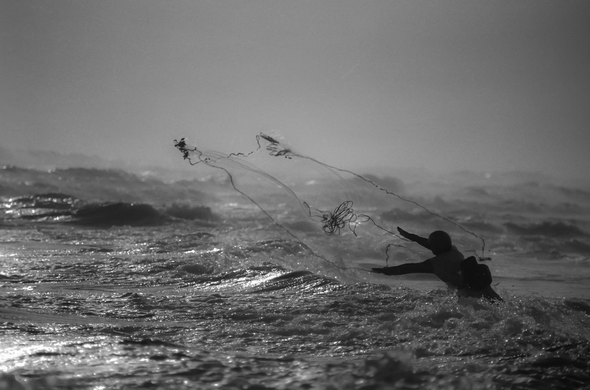 Pescatore che lancia la rete in mezzo alle onde di una spiaggia indonesiana.