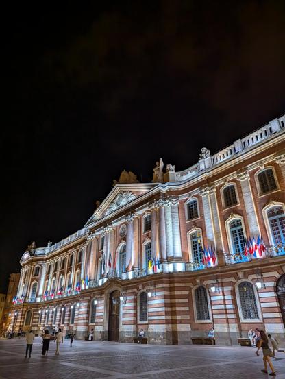 Façade de l'hôtel de ville du Capitole à Toulouse, illuminé la nuit et parsemé de drapeaux français, européens, et ukrainiens.