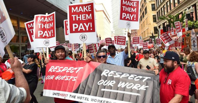 Hotel workers UNITE HERE union members march holding banner
RESPECT OUR GUESTS RESPECT OUR WORK 
And signs
MAKE THEM PAY !
