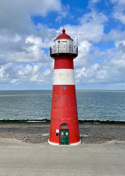 Red and white lighthouse by the sea under a partly cloudy sky.