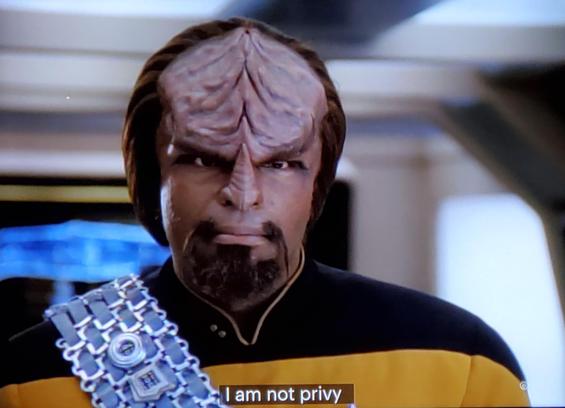 TNG scene. We're in engineering and seeing a conversation between Worf and Data. Wharf is a Klingon with ridged loaf on his forehead and a menacing goatee. Here, he's listening and looking super irritated. Data, an android with milky white skin, is speaking. Closed caption reads, "I am not privy to the exact details of when, where or how your first coupling took place. I could investigate it."