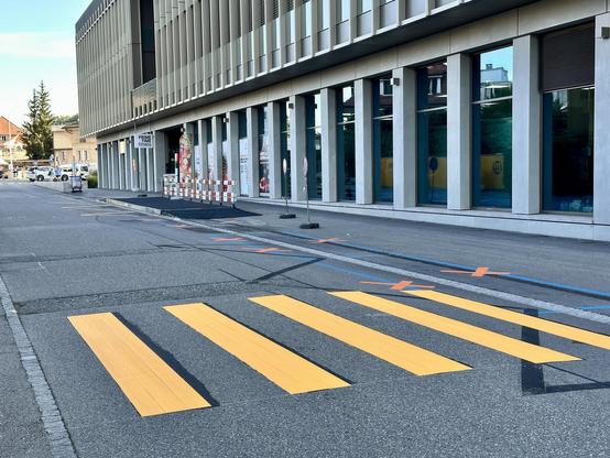 Ein neu gemalter Zebrastreifen führt über die schmale Quartierstrasse. Etwas weiter entlang der Strasse ist eine etwa 10cm hohe Bushaltestelle auf den Bürgersteig «auf-asphaltiert», inkl. Rampe.