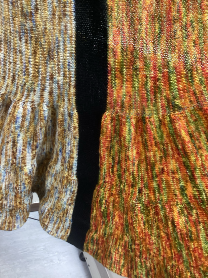 A closer picture of the two coloured sections. The one on the left is white, blue, yellow and gold. The section on the right is red, orange, green and yellow. As you move down the fabric, it becomes slightly more voluminous. The bands of colour within the sections are more clearly defined and there is a black band that separates both sections.