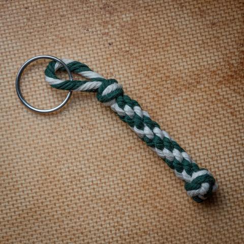 A photograph of a bellrope-style keychain pendant, tied in 3mm cotton cord in green and off-white.
