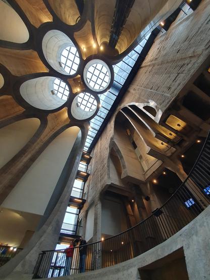 Inside of an incredible brutalist building, looking up towards a giant atrium cut out from looks like multiple tubes (used to be a grain silo).