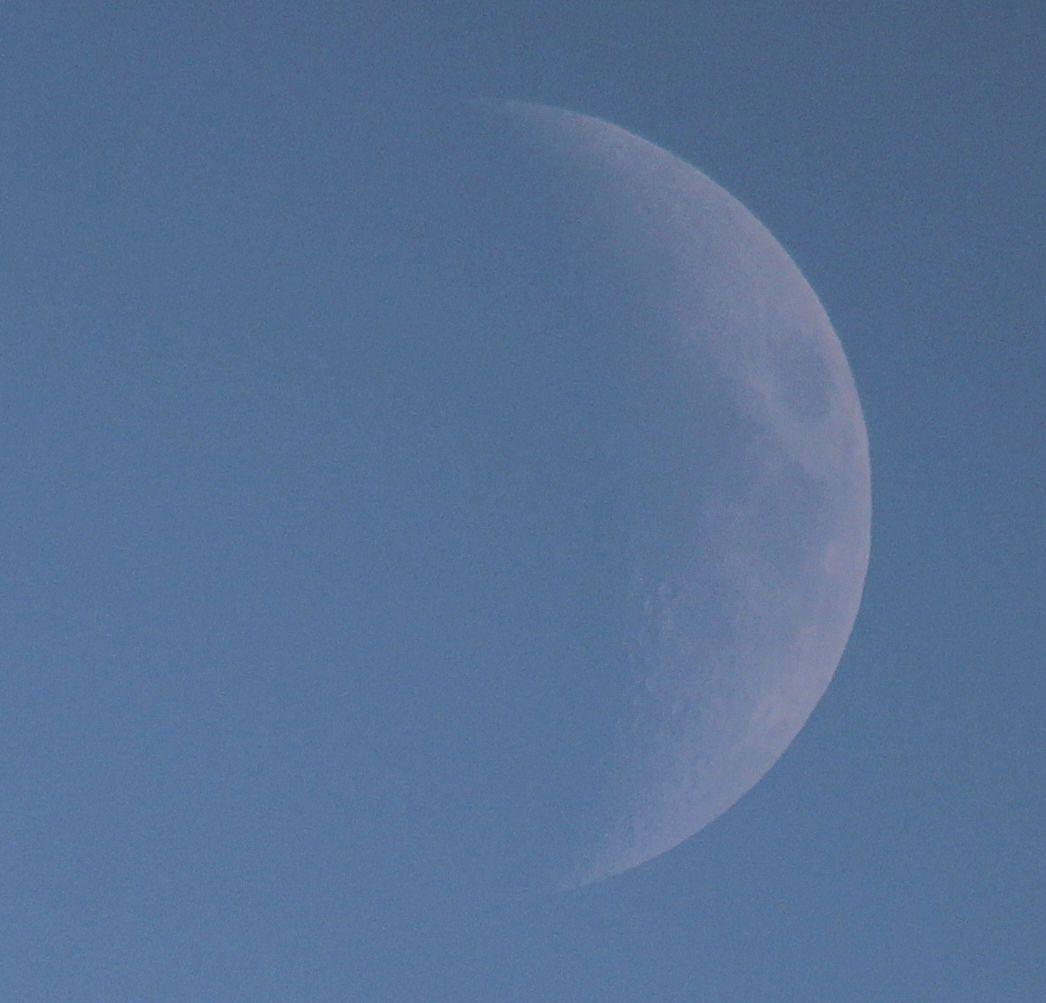 The Moon at waxing crescent phase on a blue sky background. 