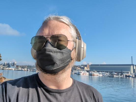 A raw photo of me with sunglasses, a black mask and black t-shirt against a blue sky.