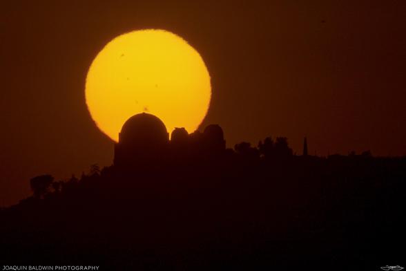 The sun setting over the silhouette of the Griffith Observatory, shot with a 500mm lens. Many sun spots are visible as dark splotches, but they aren't as sharp as they could've been.
