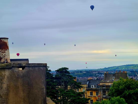 Sky, hill, roofs and 8 balloons in the air.