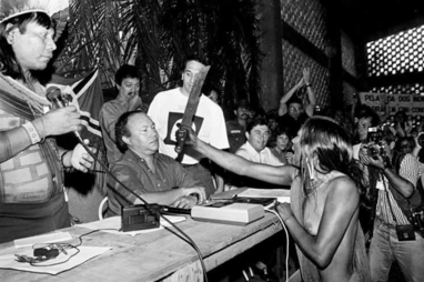 Tuíra Kayapó (1970 - 2024), indigenous warrior from the Kayapó people (Pindorama-Brasil), pointing her machete to the man responsible for the construction of a dam on her people's land (1989). May the enchantments lead your spirit back home.