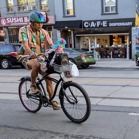 A cyclist riding a bike with a chicken of some sort on the handlebars