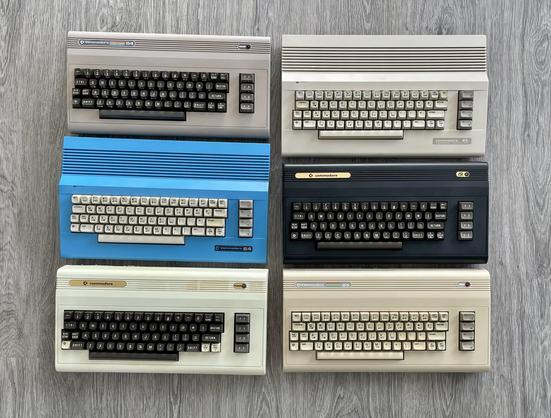 Six Commodore 64 computers in different colours and styles.