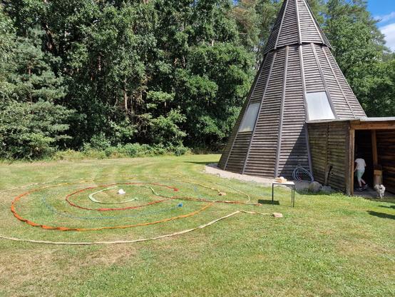 11.5 meter high wooden tipi surrounded by trees.