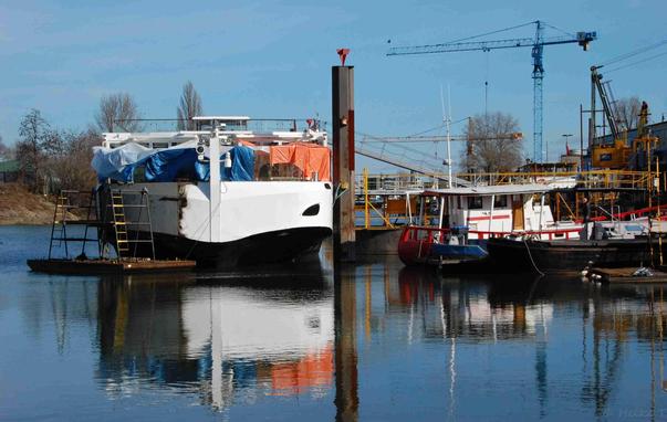 Ein Boot ist im Mülheimer Hafen angedockt, umgeben von zwei Schiffen und einem Kran im Hintergrund.