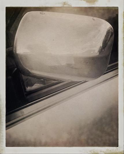 Back of a rear view mirror on a vintage car in the upper half of the rectangular frame. A vintage black and white filter has been applied.