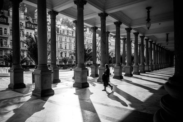 Mill Colonnade in Karlovy Vary in the morning with sunlight creating shadows and a person walking through the frame