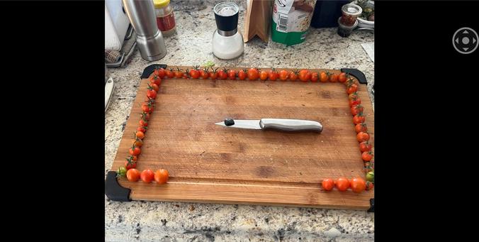 Many sungold little orange tomatos arranged around the drip channel of a retangular bamboo? Cutting board with a six inch paring knife with a gram of hash on the knife