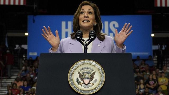 Kamala Harris giving campaign speech at podium in Las Vegas, NV. I'm in the background of the photo in the bottom right corner. Out of focus white woman in a blue tank top. 
[AP Photo/Julia Nikhinson]