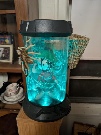 An Alien Romulus collector bucket resembling an Alien canister with a facehugger crawling on the outside. Inside is a large vinyl figure of Marvin the Martian  watching the facehugger.